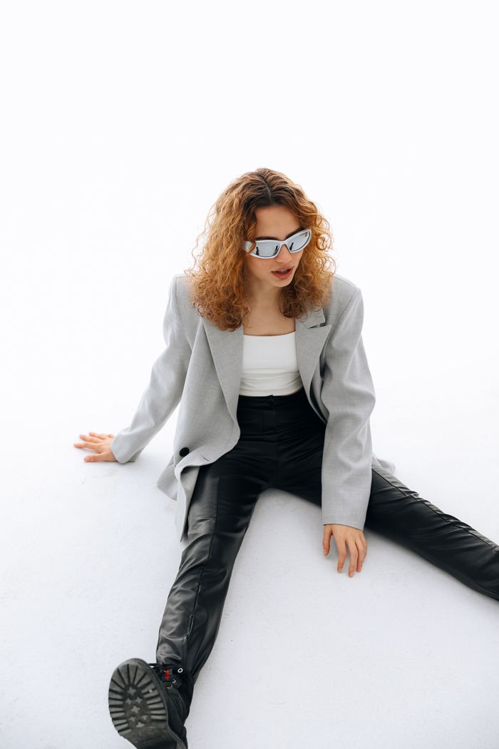 Woman in trendy outfit sitting on white floor, wearing edgy sunglasses for fashion look.