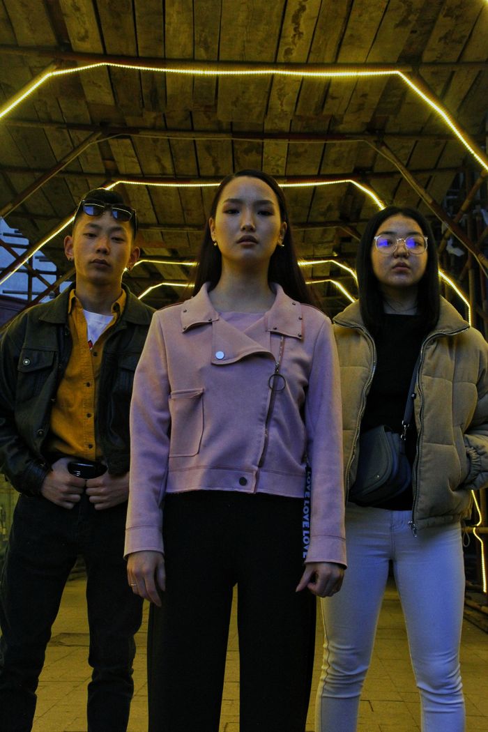 Home From below of young Asian friends in stylish clothes standing on street under roof with bright illumination